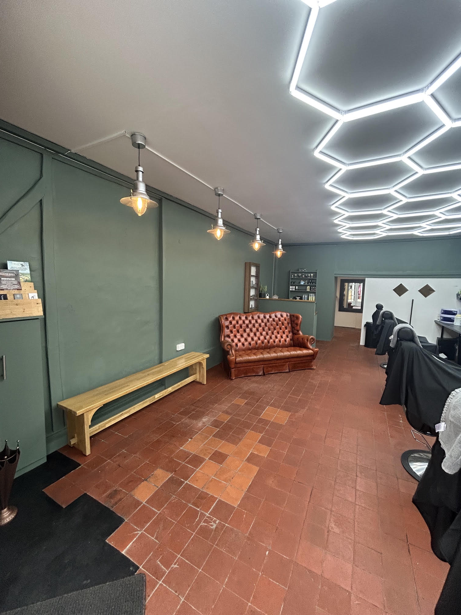 The waiting area with a wooden bench and leather Chesterfield under pendant lights